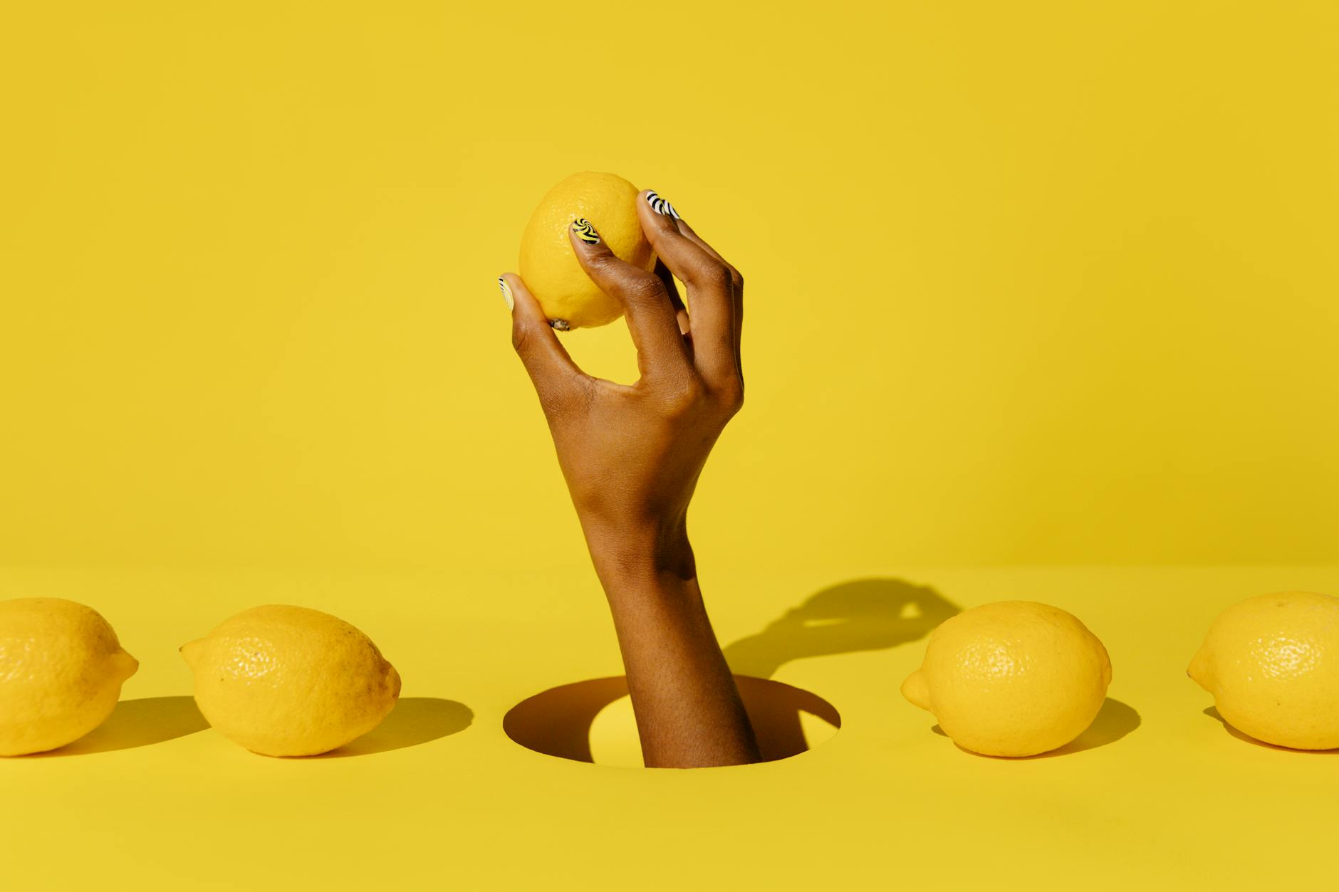 A hand holding a lemon against a vivid yellow background, conveying freshness and citrus vitality
