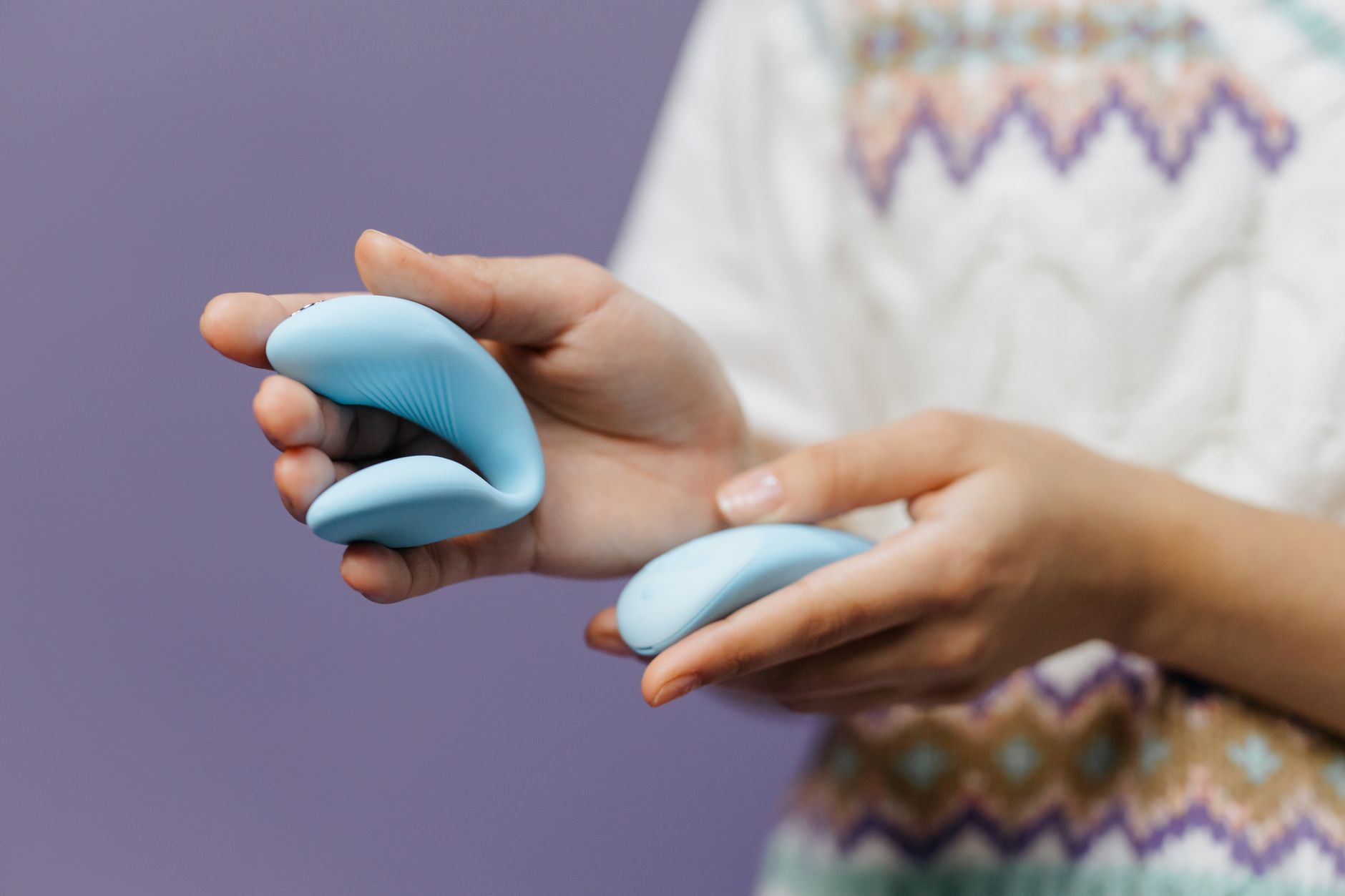 Close-up of hands holding a sleek blue vibrator against a purple background.