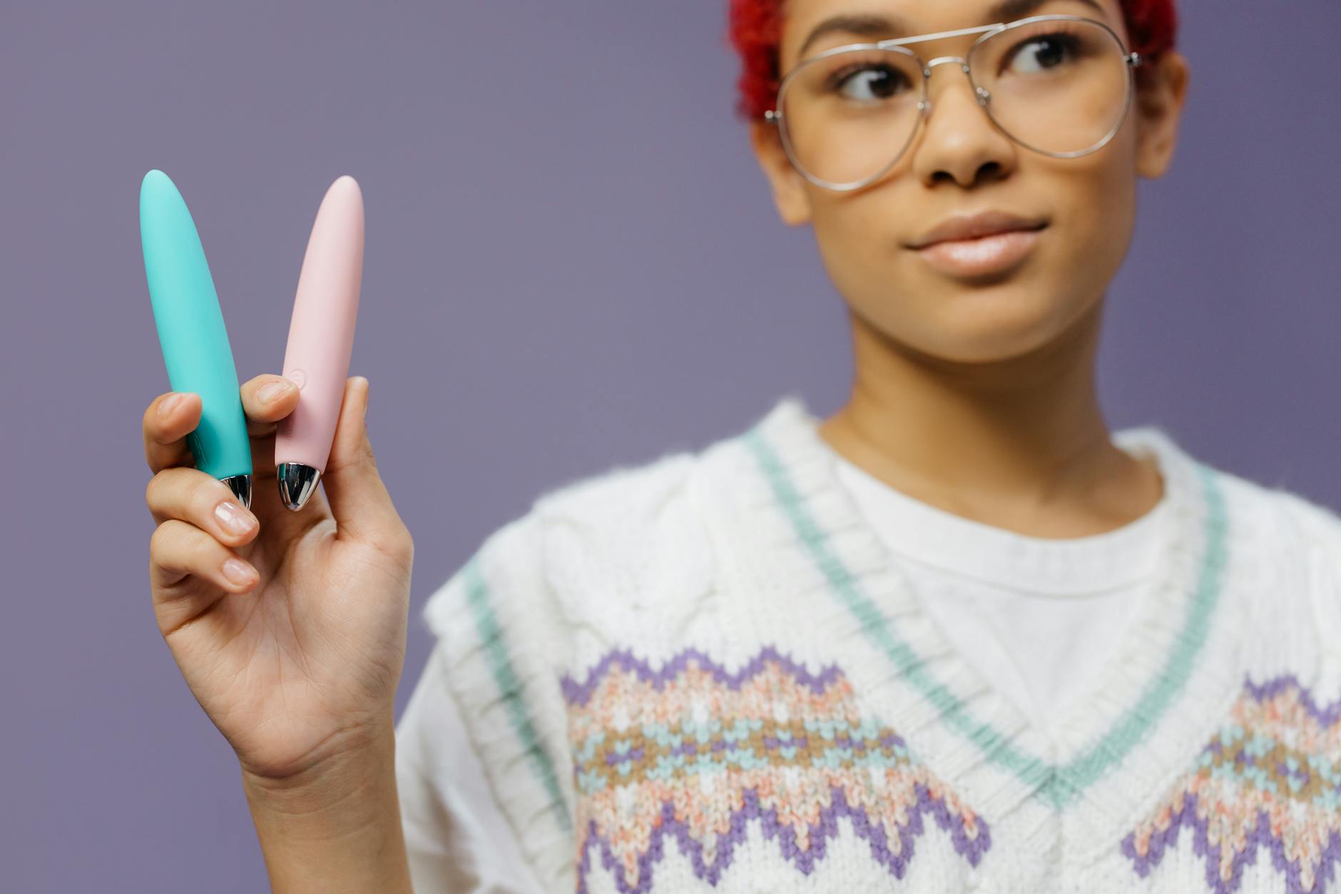 A woman holding two vibrant yellow silicone vibrators against a purple background, symbolizing cycle-aware pleasure practices.