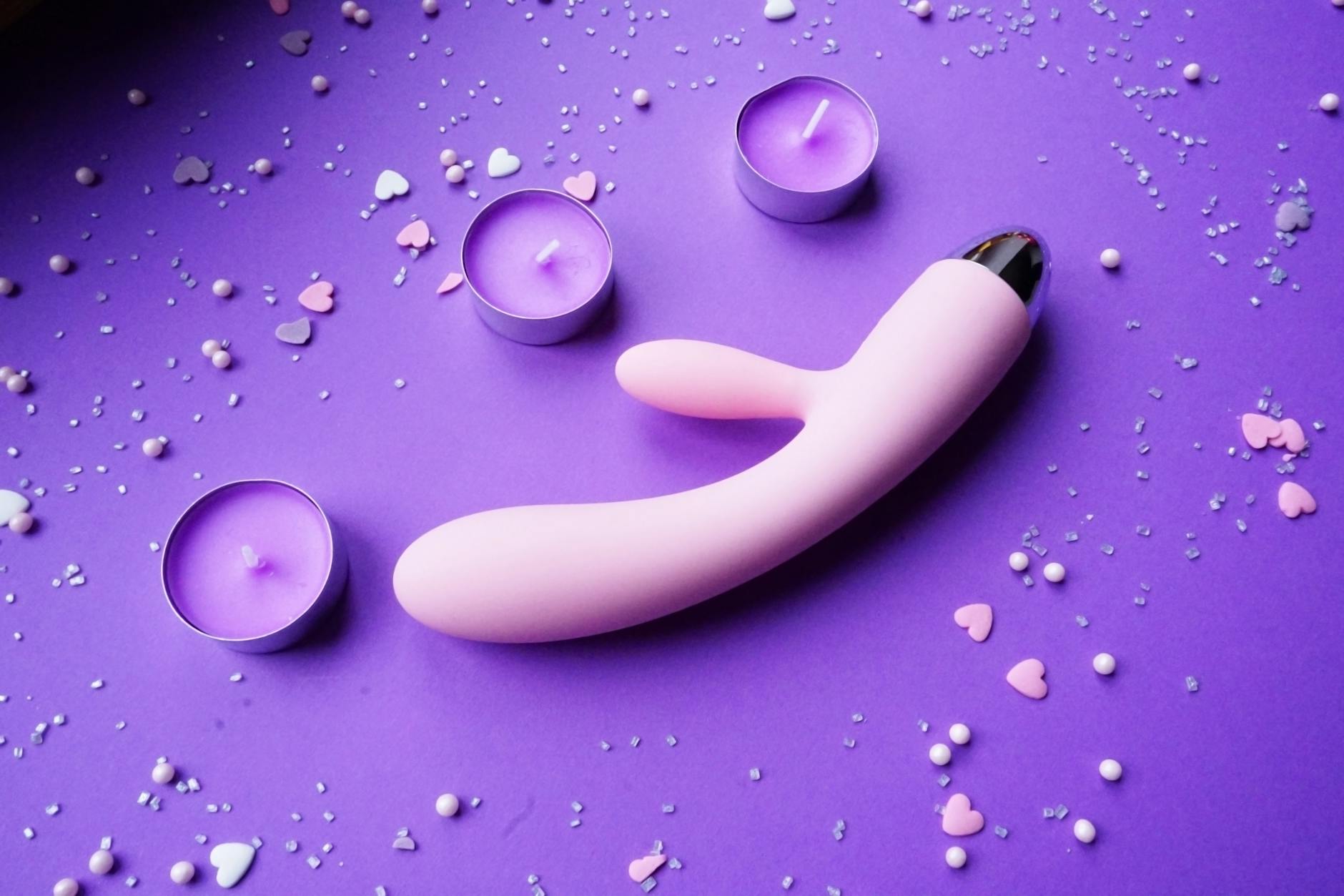 A blue silicone clitoral vibrator held in hand against a purple background, symbolizing self-love and open sexuality.