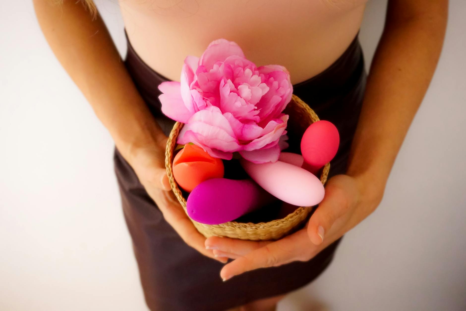 A person holding a basket with colorful vibrators and fresh flowers on white background